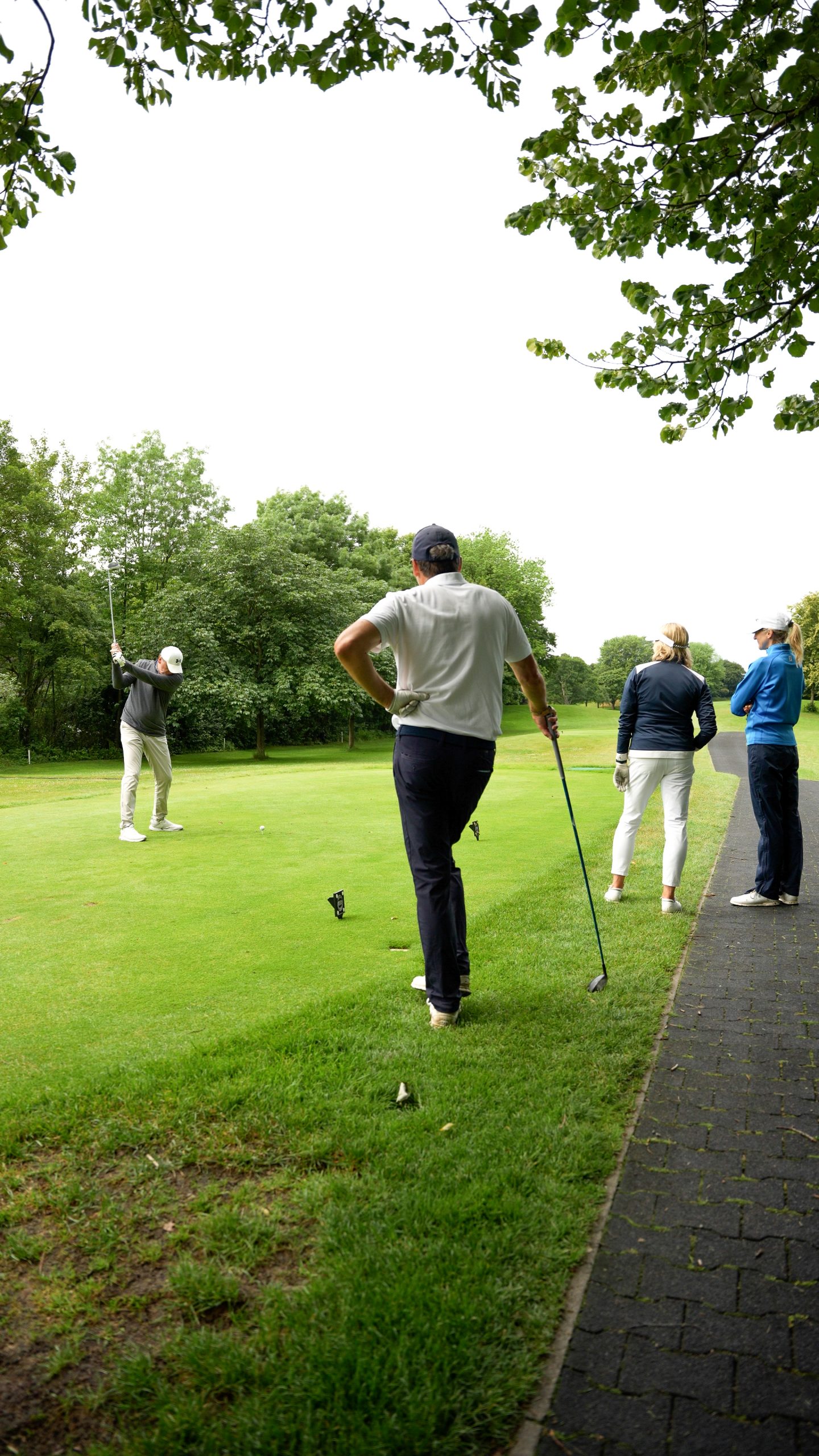 3 Golfer sehen einen Mitspieler beim Abschlag zu auf dem APS Charity Golfturnier