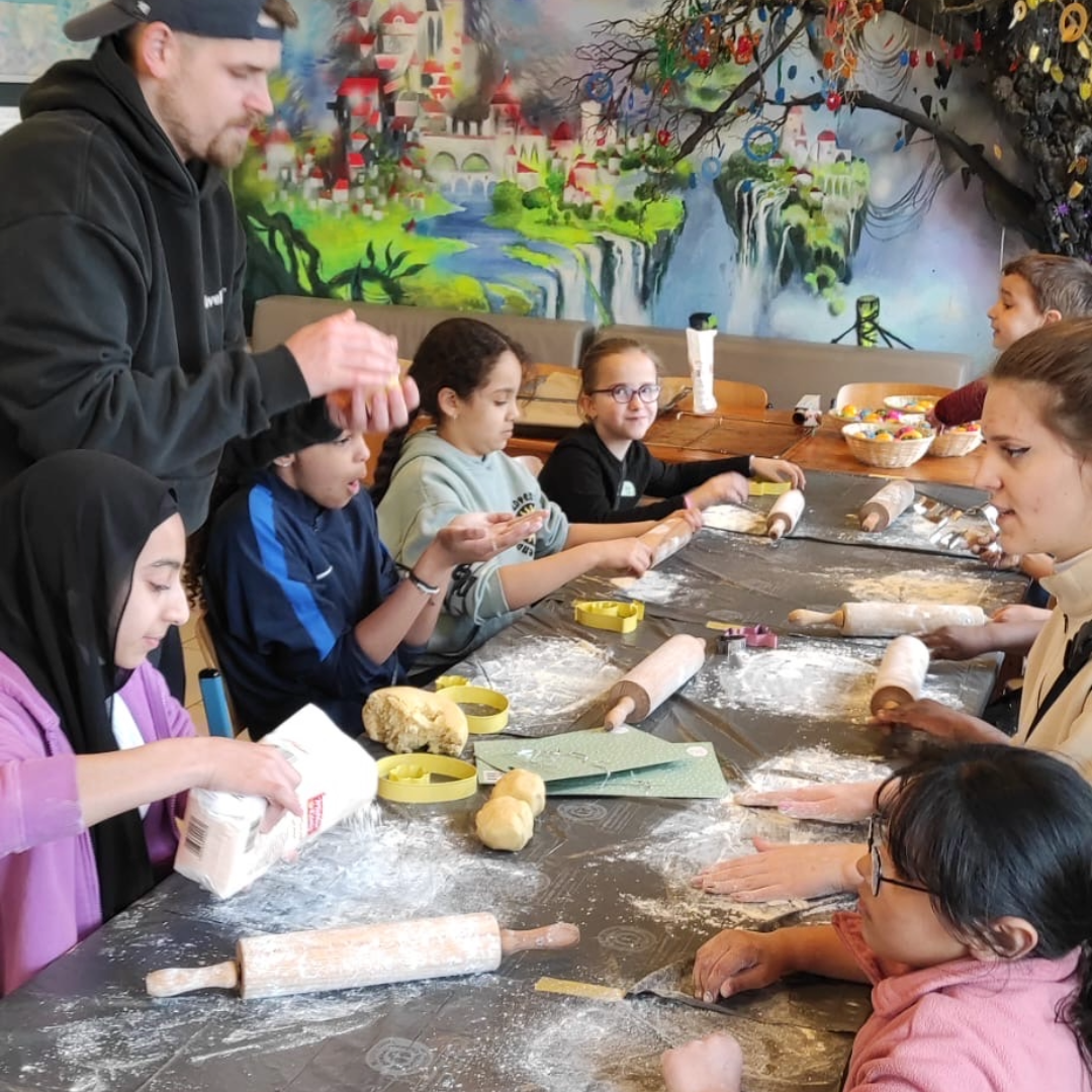 Kinder und Erwachsene beim Keksebacken, mit Teig und Ausstechformen auf einem Tisch.