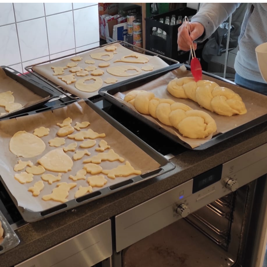 Ungebackene Plätzchen und Hefezopf auf Backblechen. Eine Person bestreicht den Zopf.