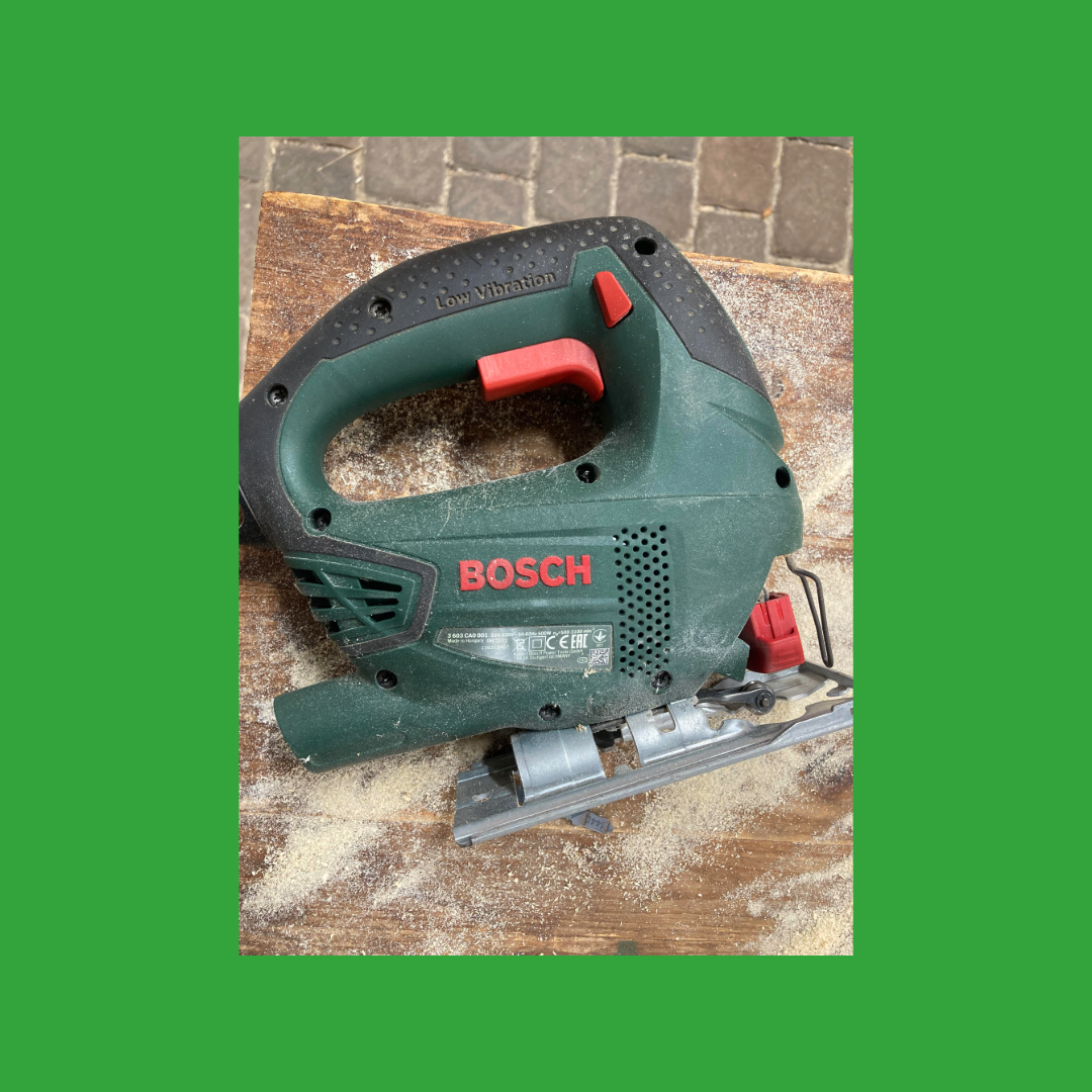 Grüne Bosch Stichsäge auf einem Holztisch mit Sägespänen.