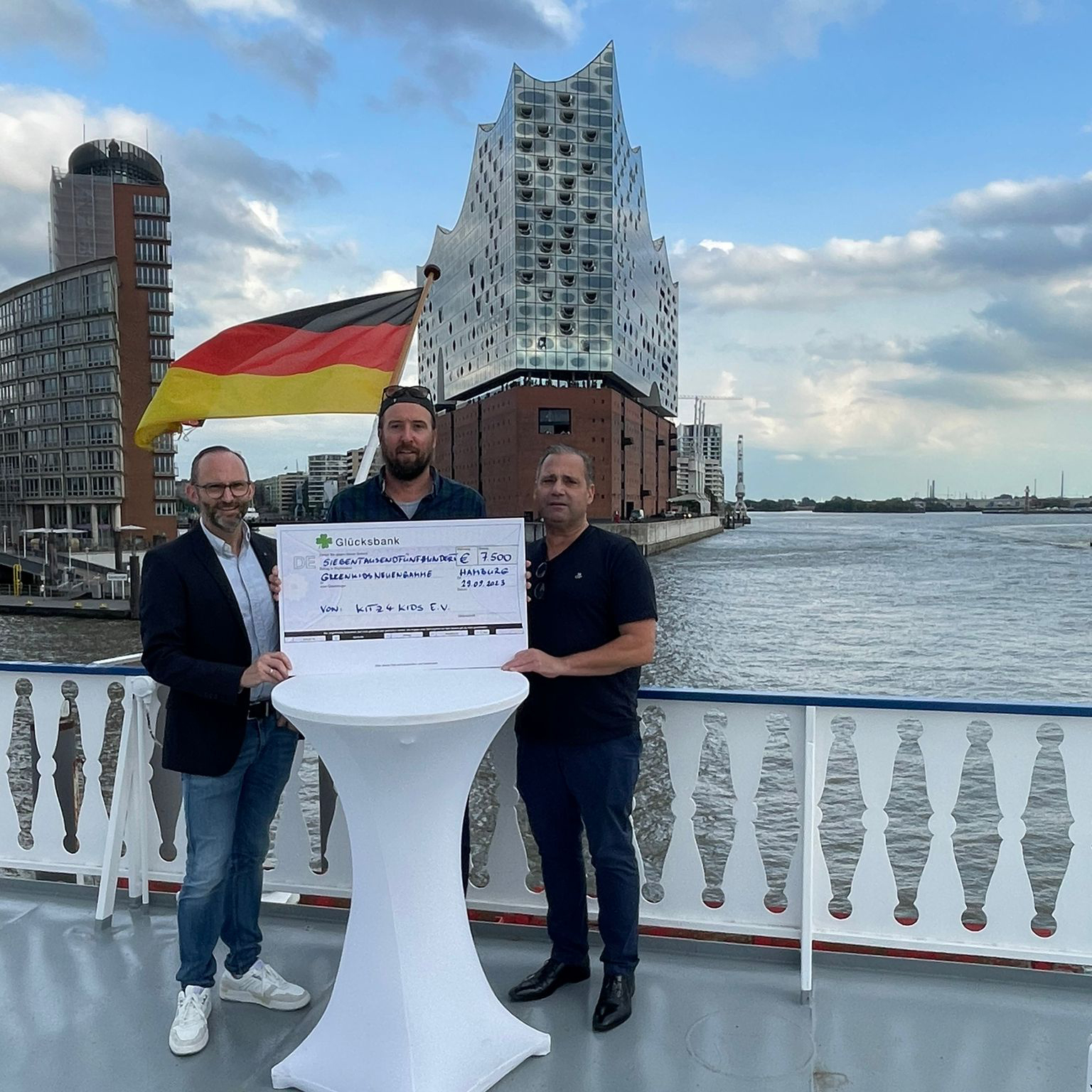 Personen stehen an einem Tisch im Freien mit Blick auf den Hamburger Hafen.