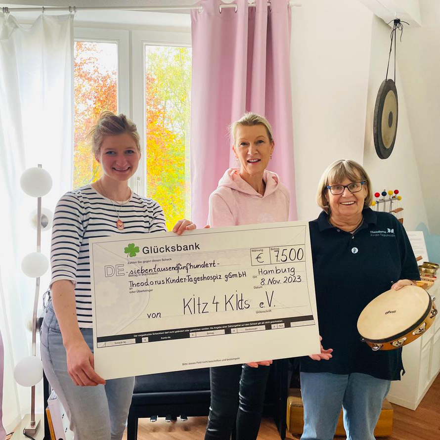 Drei Personen halten einen Scheck in einem Wohnzimmer.